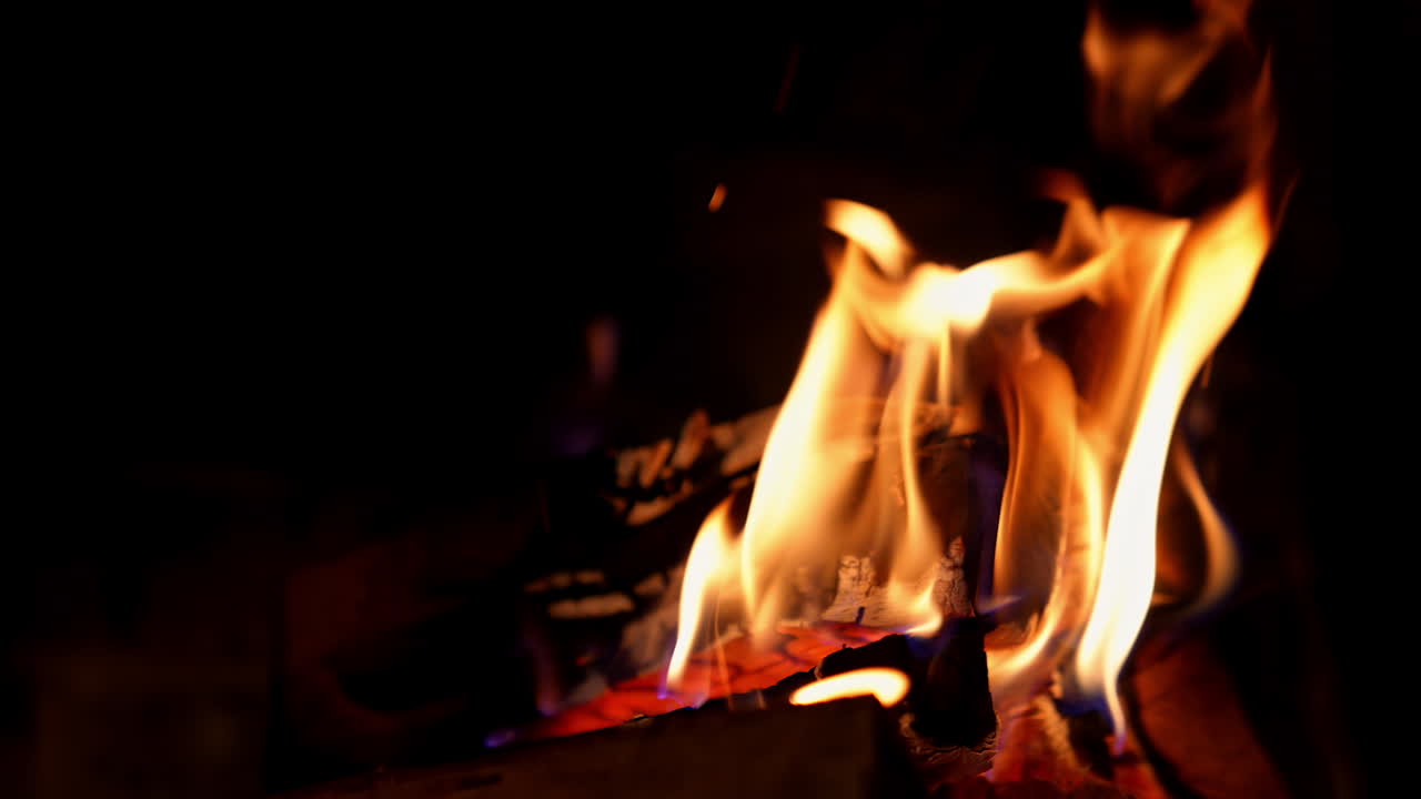 Orange flame in fireplace on black background. Wooden logs in fire flame. Warm cosy fire burning in fireplace. Close-up.