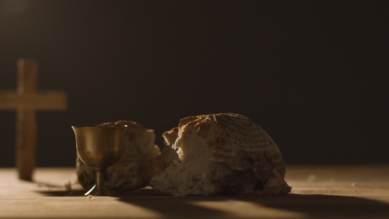 concepto religioso filmado con cáliz pan roto cruz y vino sobre mesa de madera contra fondo negro 3