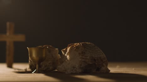 concepto religioso filmado con cáliz pan roto cruz y vino sobre mesa de madera contra fondo negro 3