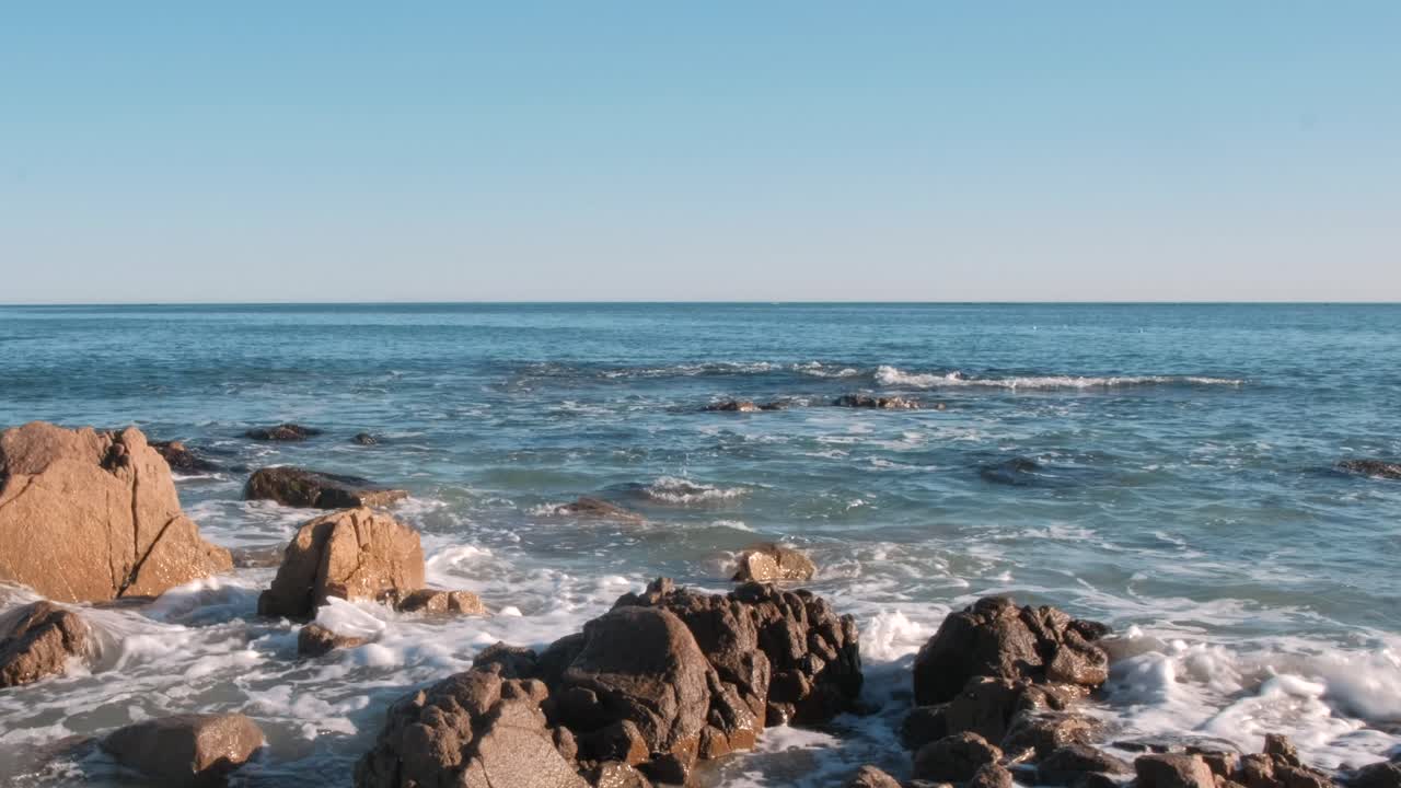 olas rompiendo suavemente en las rocas del océano con ballenas saltando en la lejanía