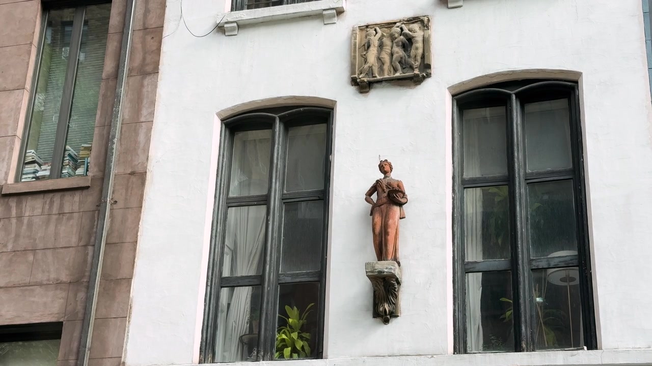 Fasade med menneskestatue og relieff over buede vinduer på utsiden av en bybygning