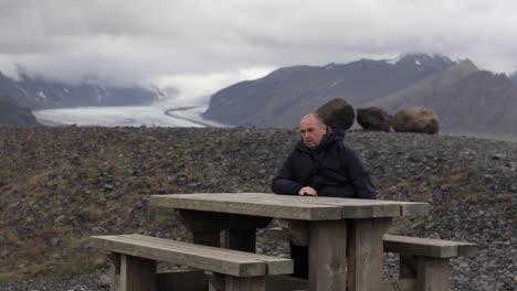 man sitting at picnic table with a mountain in the background