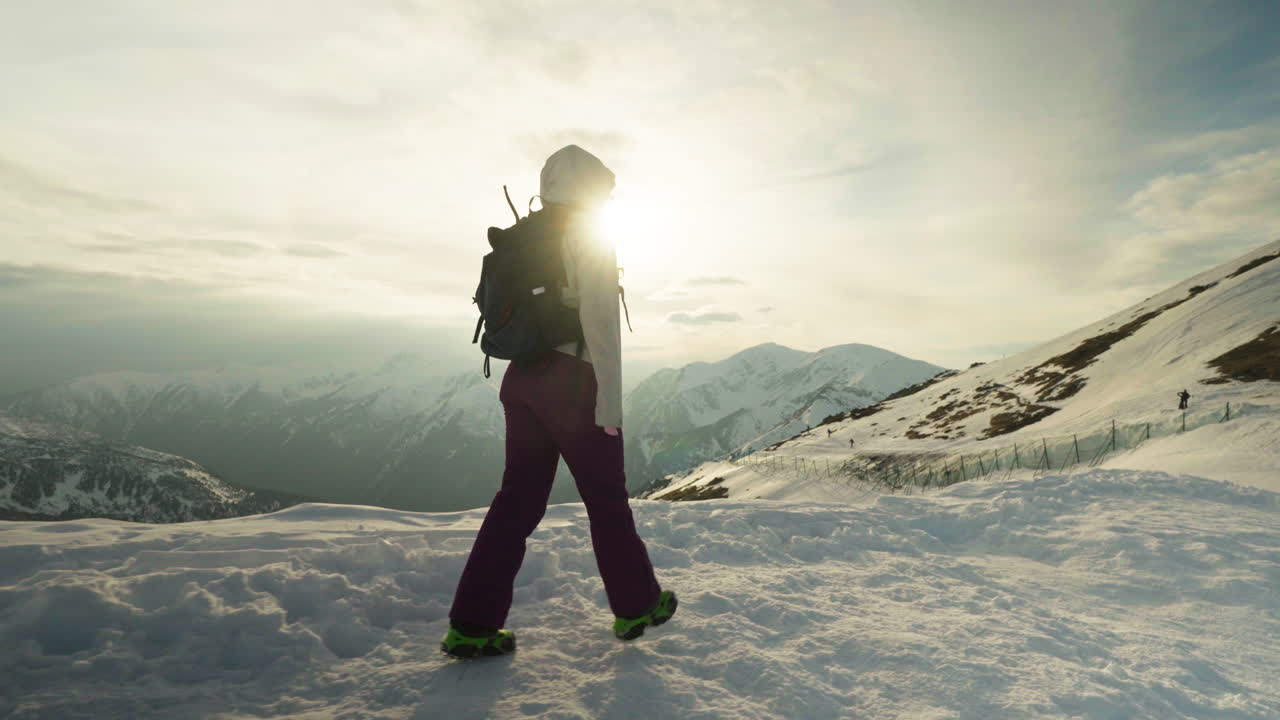 Pan shot of woman on top of snowy mountain hiking with beautiful sunset, gimbal shot