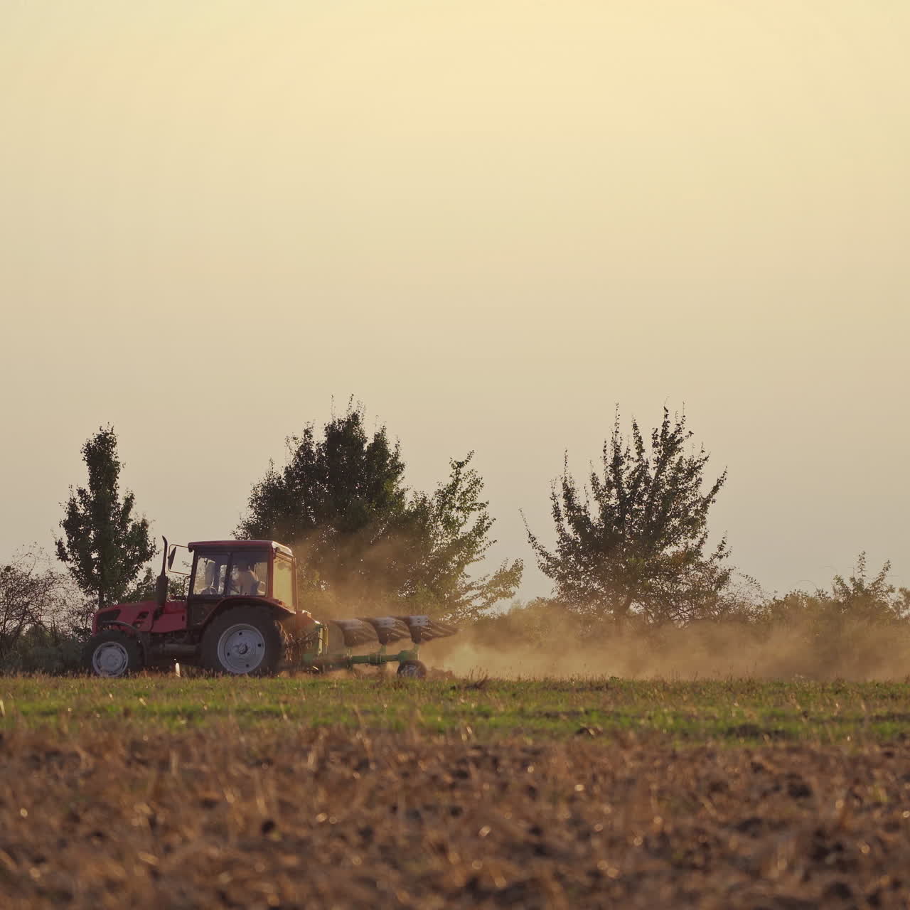 Tractor in the field in rural place. Agricultural machinery on the soil during seasonal works. Tractor cultivates the ground in the evening.