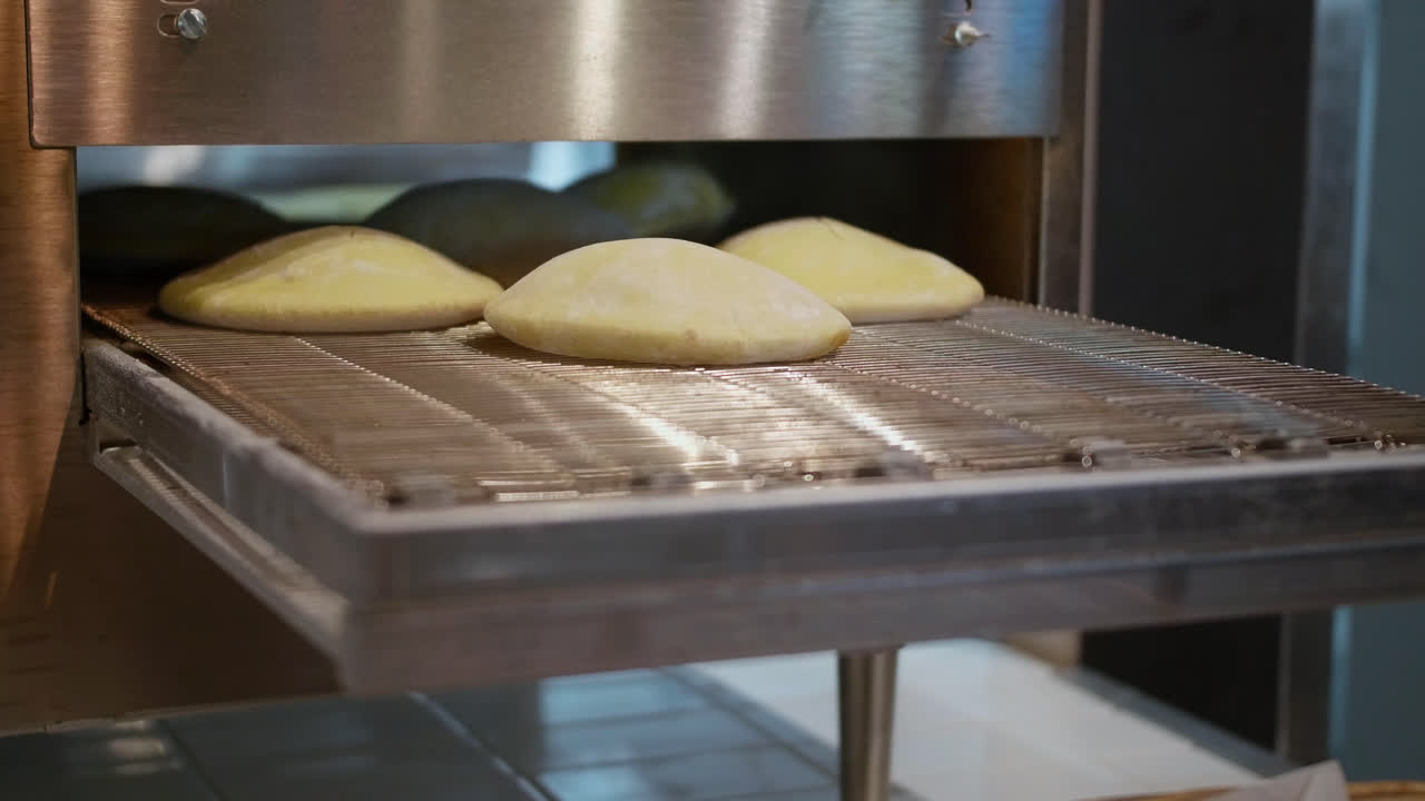 Close up, Homemade Pita on conveyor belt grill puffing up as they cook