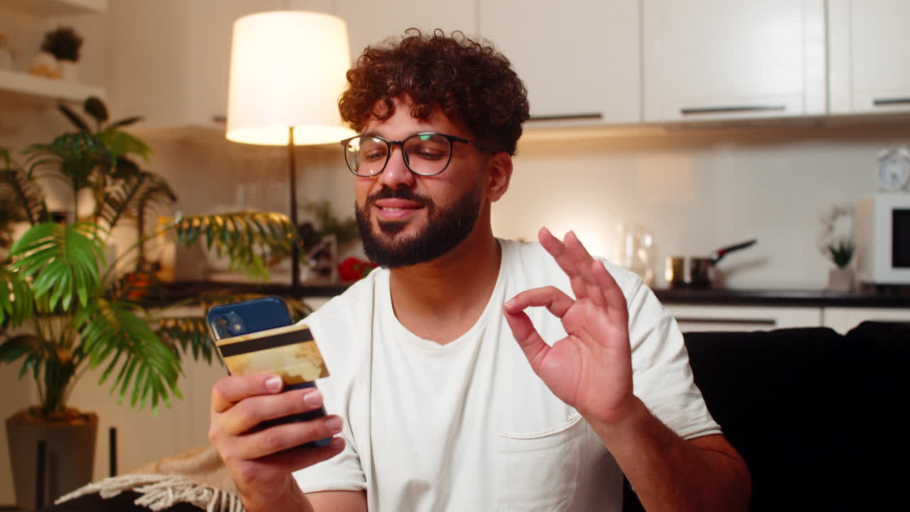 Arabisk mann godkjenner nettbetaling på smarttelefon, kort verifisert, ser rabatt, smiler, beholder kvittering