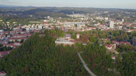 Vista-Aérea-Sobre-La-Emblemática-Torre-Glokenturm-En-El-Parque-Forestal-De-La-Cima-De-La-Colina-Schloßberg-De-Graz,-Panorámica-Del-Paisaje-Urbano