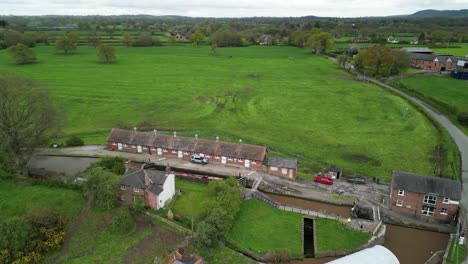 Narrowboat-entering-Bunbury-Staircase-Locks,-Shropshire-Union-Canal,-Cheshire,-England---Aerial-drone-anti-clockwise-pan,-May-23