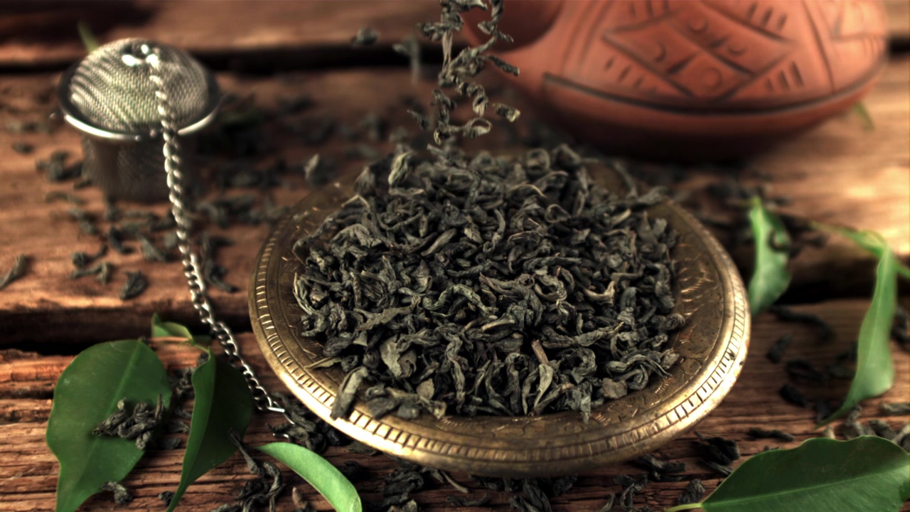 Dried Green Tea Leaves Falling into a Golden Bowl