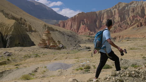 a man treks around upper mustang nepal looking at red cliff mountain and adventurous landscape scenarios around