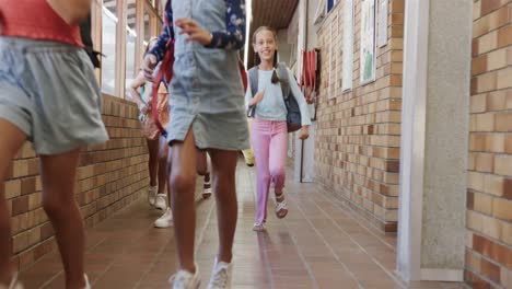 Happy-diverse-schoolgirls-with-school-bags-running-in-corridor-at-elementary-school
