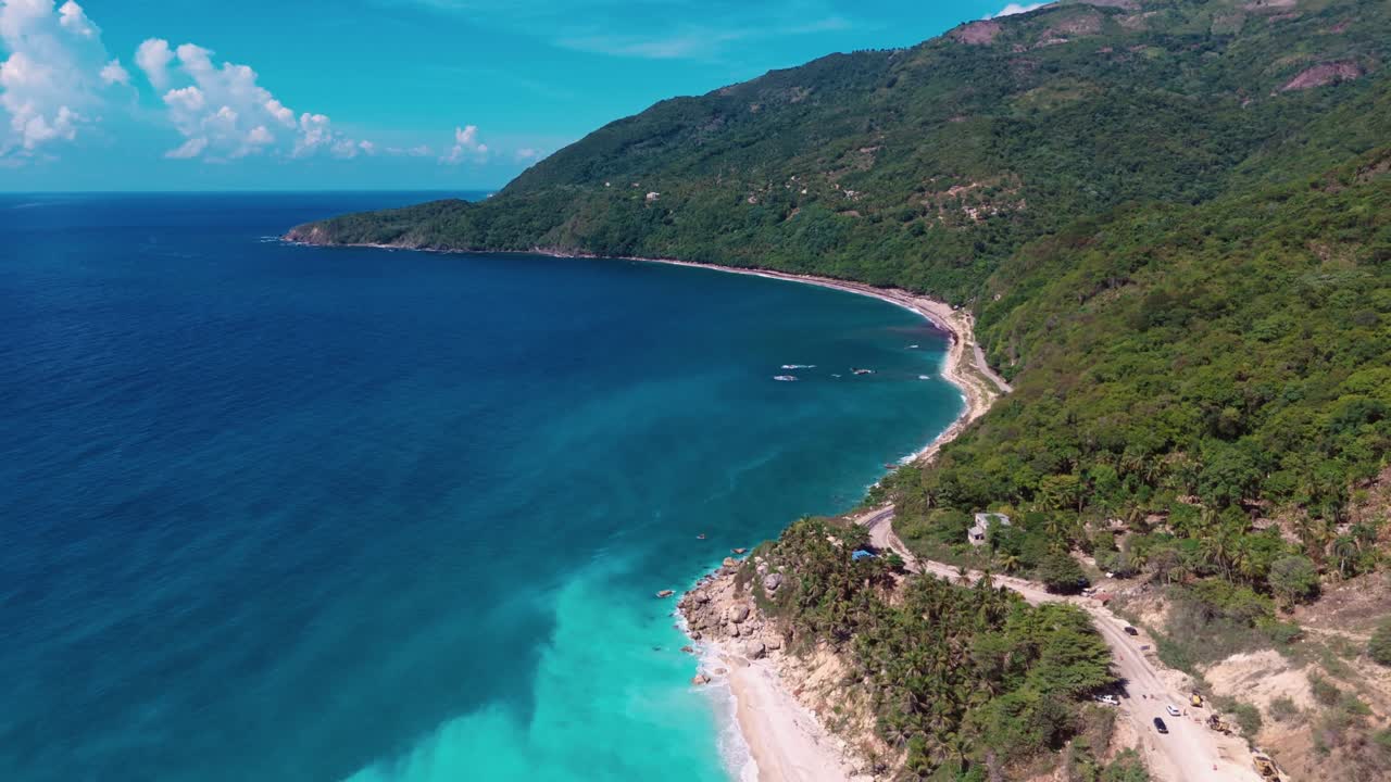 High aerial drone view of scenic coastal road next to turquoise Caribbean Sea, with lush green mountains, Barahona, Dominican Republic