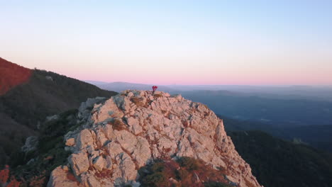 Parallaxe-Drohnenaufnahme-Einer-Frau-Beim-Yoga-Auf-Einem-Berg-Mit-Den-Ersten-Lichtern-Des-Sonnenaufgangs