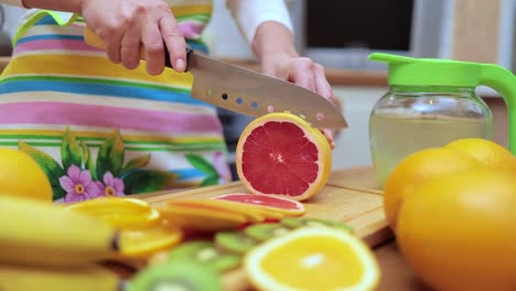 Women's-hands-Housewives-cut-with-a-knife-fresh-grapefruit-on-the-cutting-Board-of-the-kitchen-table