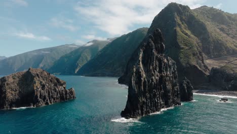 frontal aerial of ilhéus da ribeira da janela’s dramatic sea stacks, framed by emerald waters and lush cliffs along madeira’s northern coast.