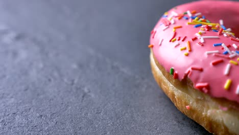 un primer plano de una deliciosa rosquilla rosada con patatas fritas multicolores y ojos girando lentamente sobre el fondo gris de la mesa.