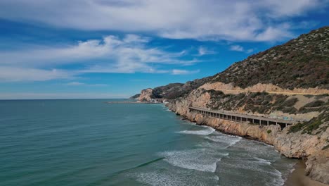 The-coastal-road-and-scenic-coastline-of-port-ginesta,-barcelona,-aerial-view