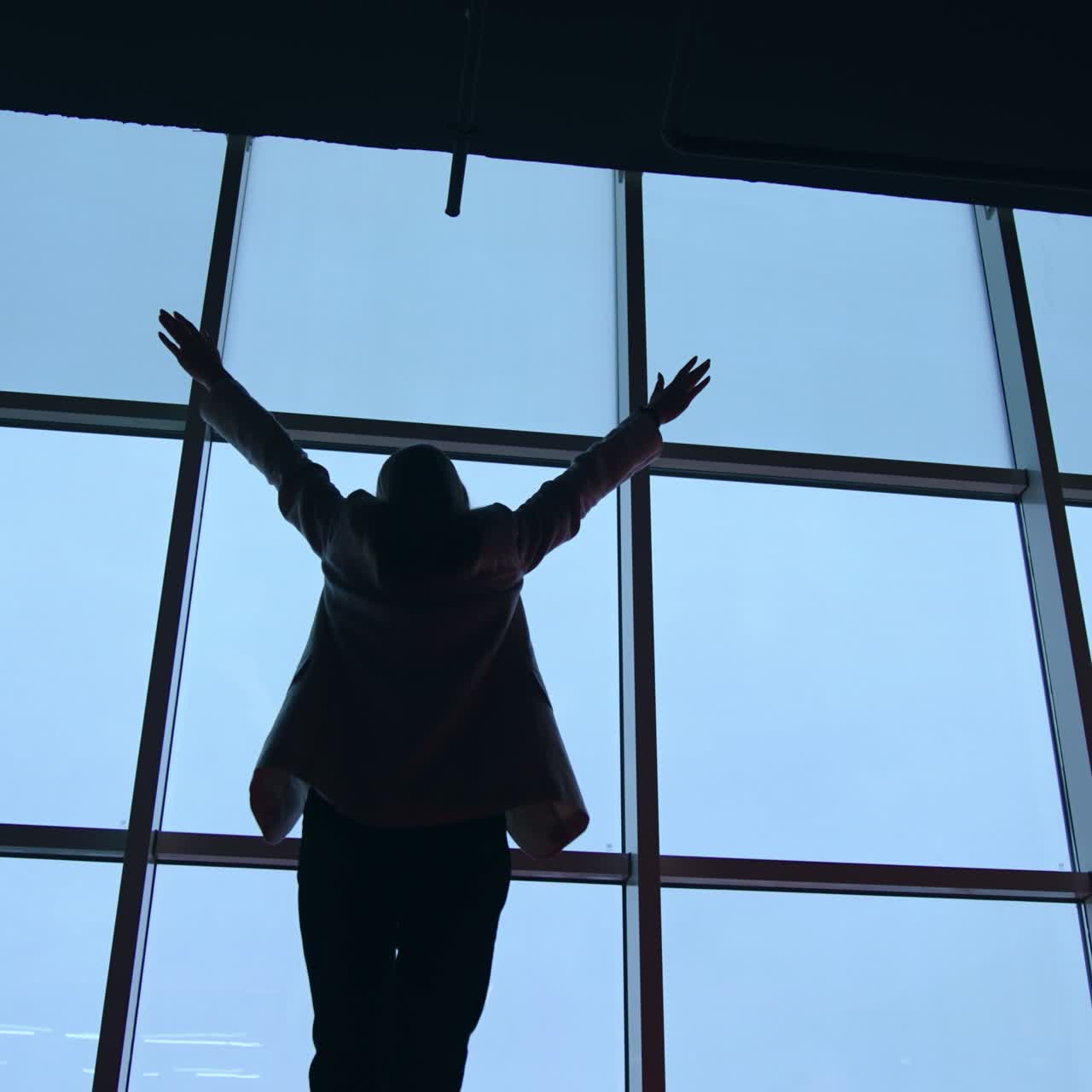 Lady in jacket and trousers comes up to the panoramic window. Dark female silhouette rises hands happily at the window