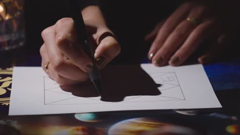 close up of woman drawing astrology lagna or birth chart on candlelit table 6