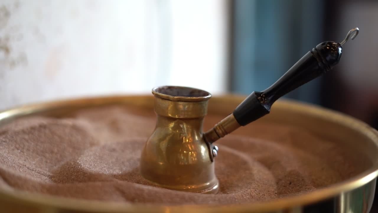 A coffee pot brewing over hot sand, close up shot