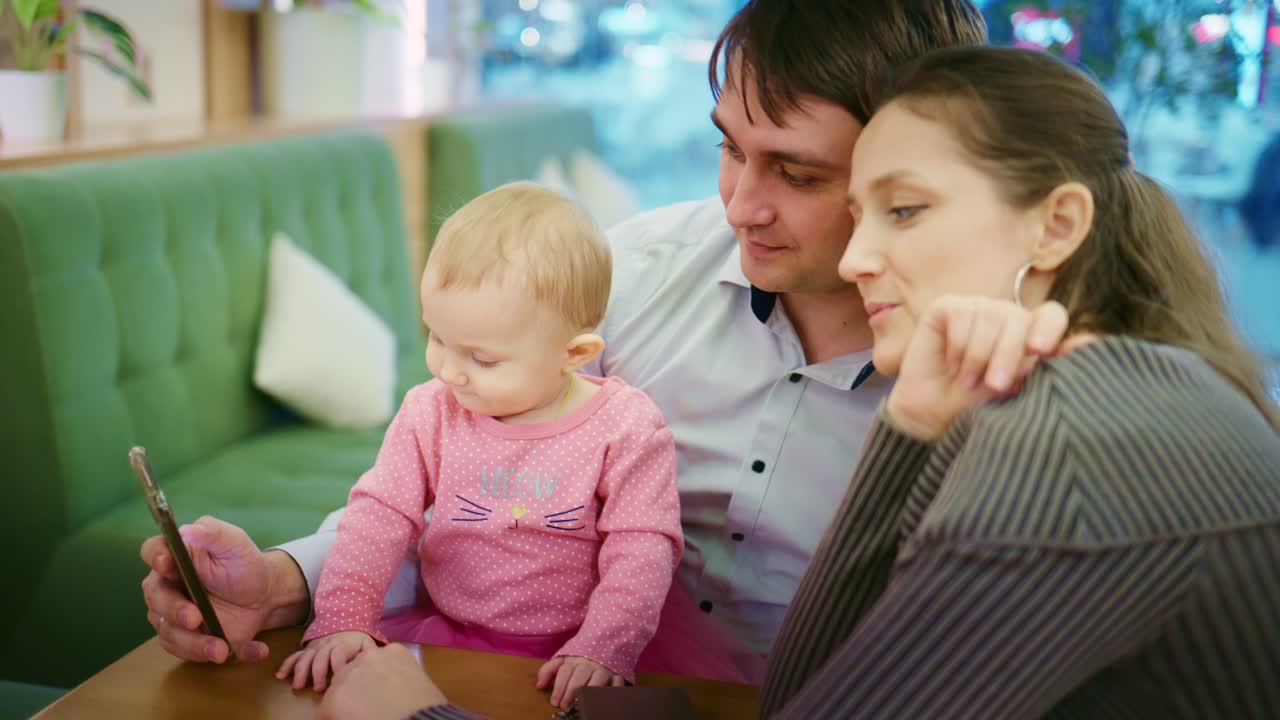 Giovane famiglia con bambino che guarda lo smartphone al bar