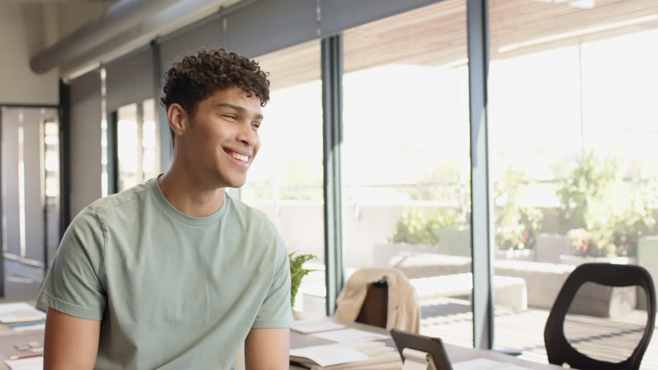 Smiling young man in modern office, sitting at desk with laptop and documents, copy space