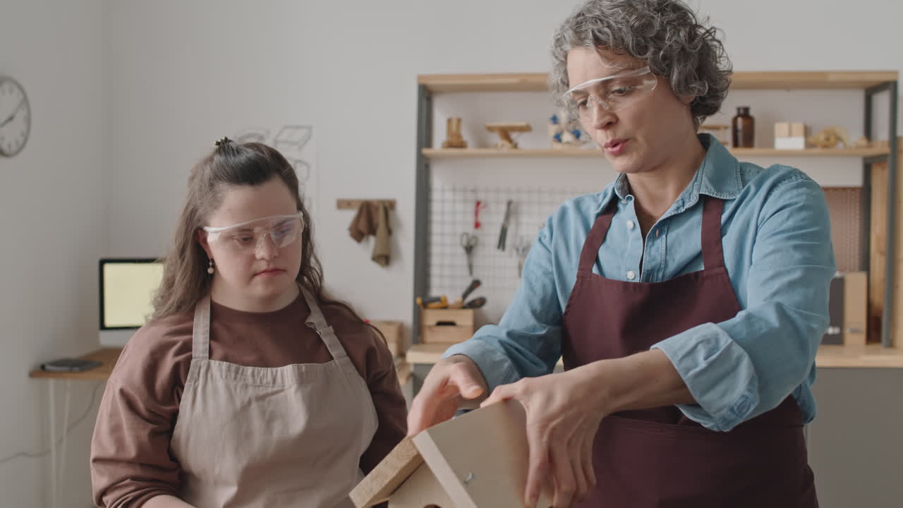 A woman is teaching another woman how to build a birdhouse
