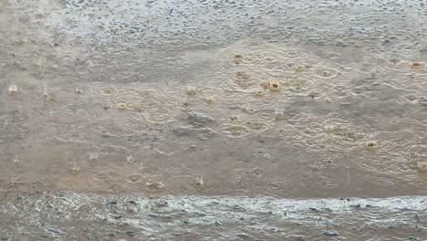 closeup of a heavy rain droplets falling on the puddle of water on concrete creating ripples and small splashes