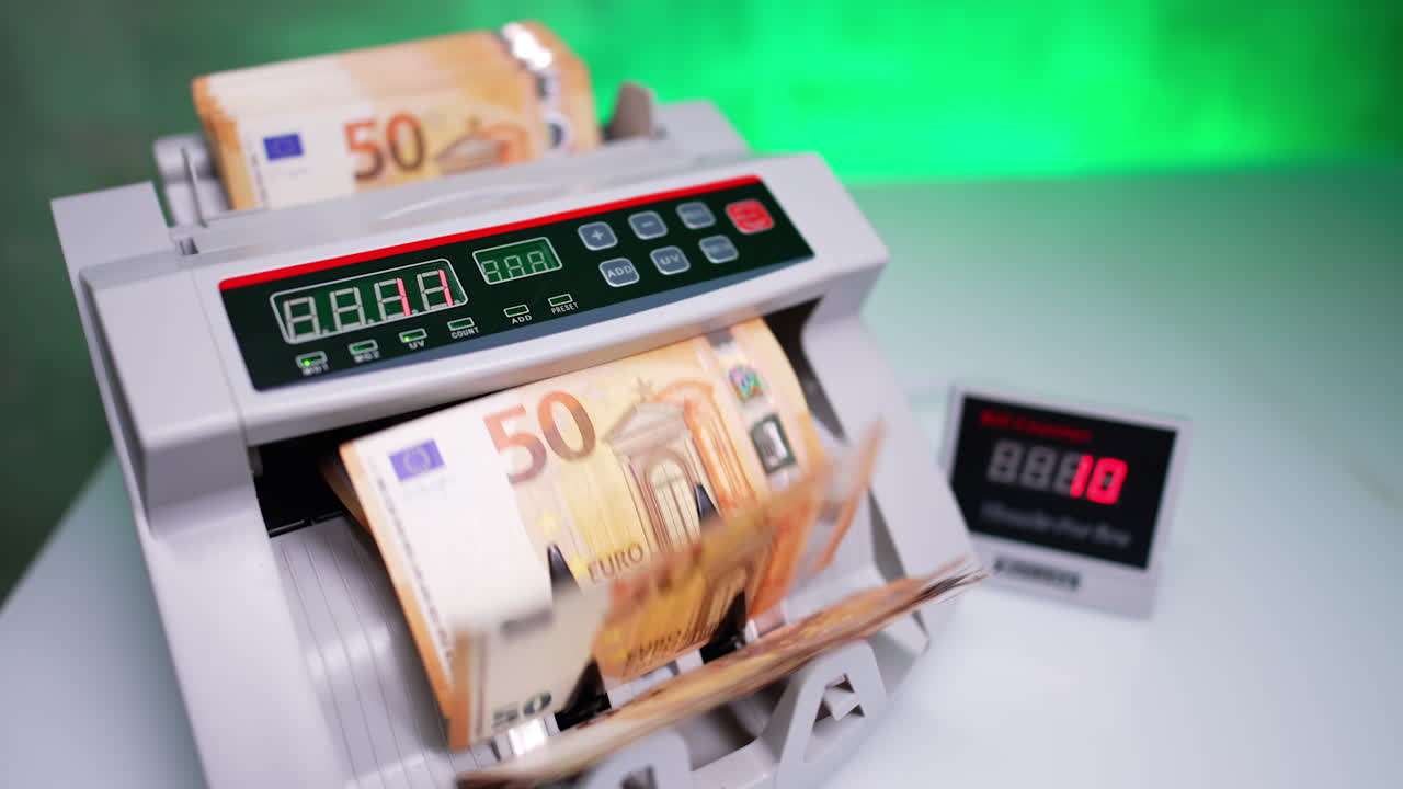 Female hand puts money stack into cash counting machine and its blades start rotating. Woman pushes the bills and they are counted in equipment. Top view close up.