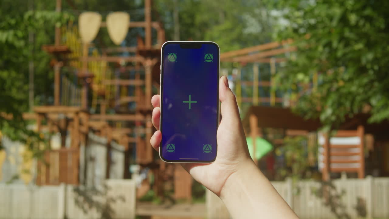Young woman holding phone chroma key screen in front of playground close-up. Girl with green screen on smart phone. Nature