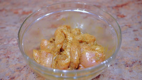 carne de pollo marinada con especias en un recipiente de cristal encima de una mesa de mármol