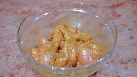 marinated chicken meat with spices in a crystal glass bowl on top of a marble table