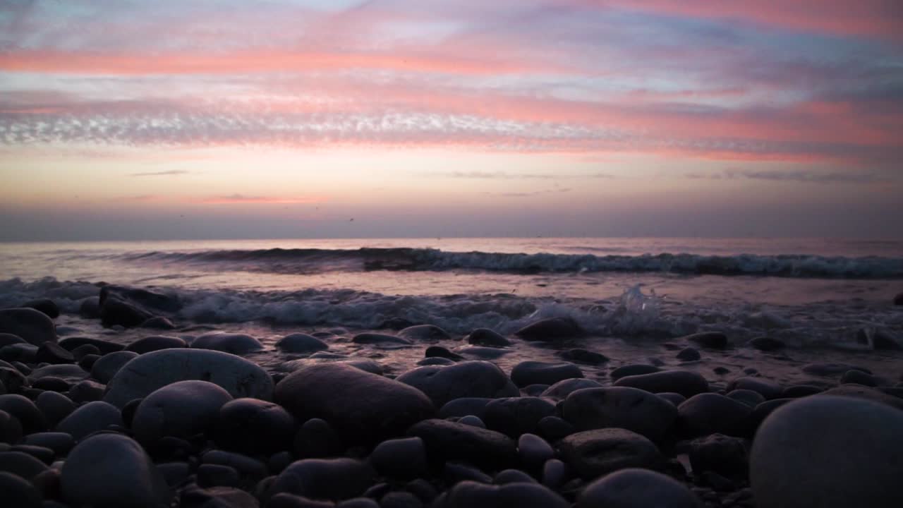 Calm waves hitting a round rock beach in a colorful sunset. Slowmotion
