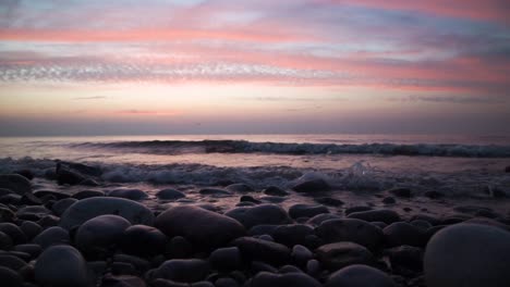 calm waves hitting a round rock beach in a colorful sunset. slowmotion
