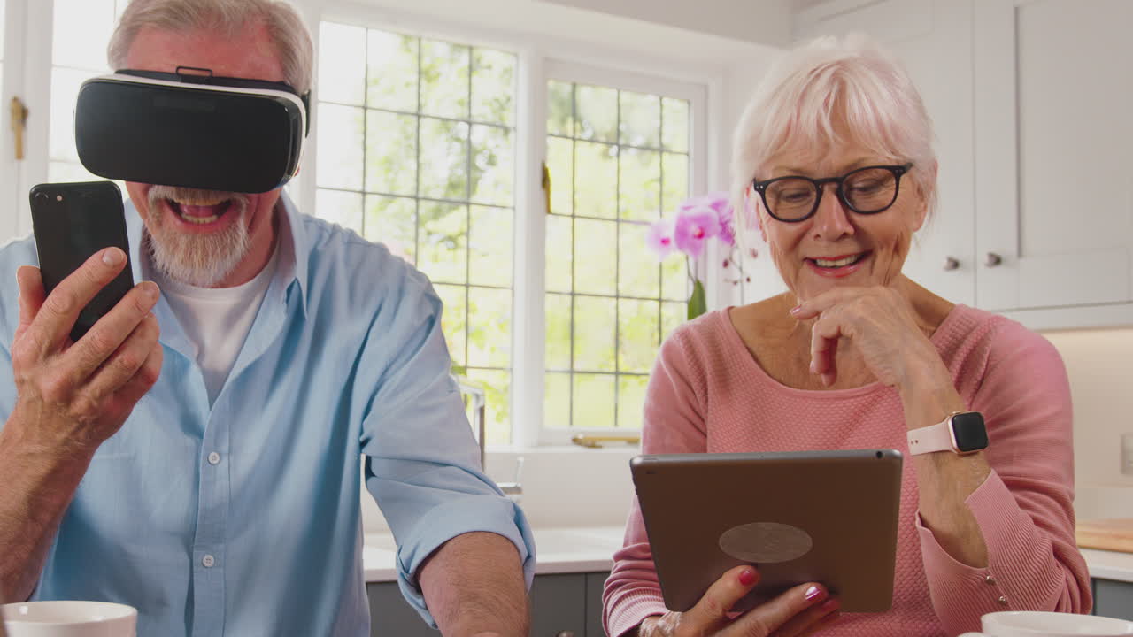 Coppia di anziani in pensione a casa che usa la tecnologia digitale con tablet, visore VR, smartwatch e smartphone