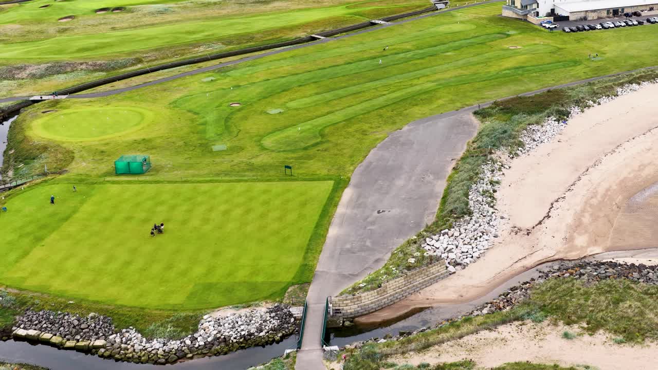 Drone glides over lush golf course, golfers on green, sandy beach, bright daylight, smooth movement