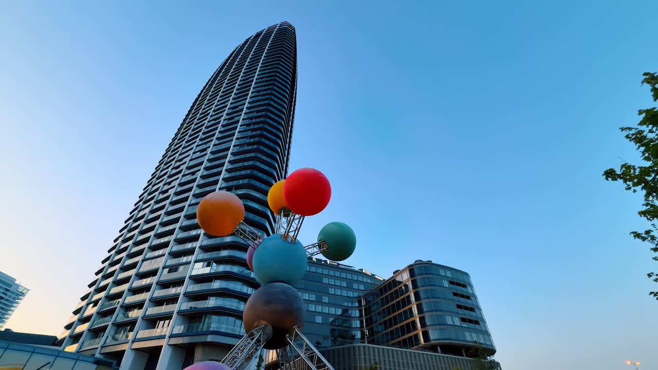 Bratislava, Slovakia - June 5, 2025: Vibrant sculpture by skyscraper. A vibrant sculpture with colorful spheres stands tall beside a modern building at sunset in an urban area