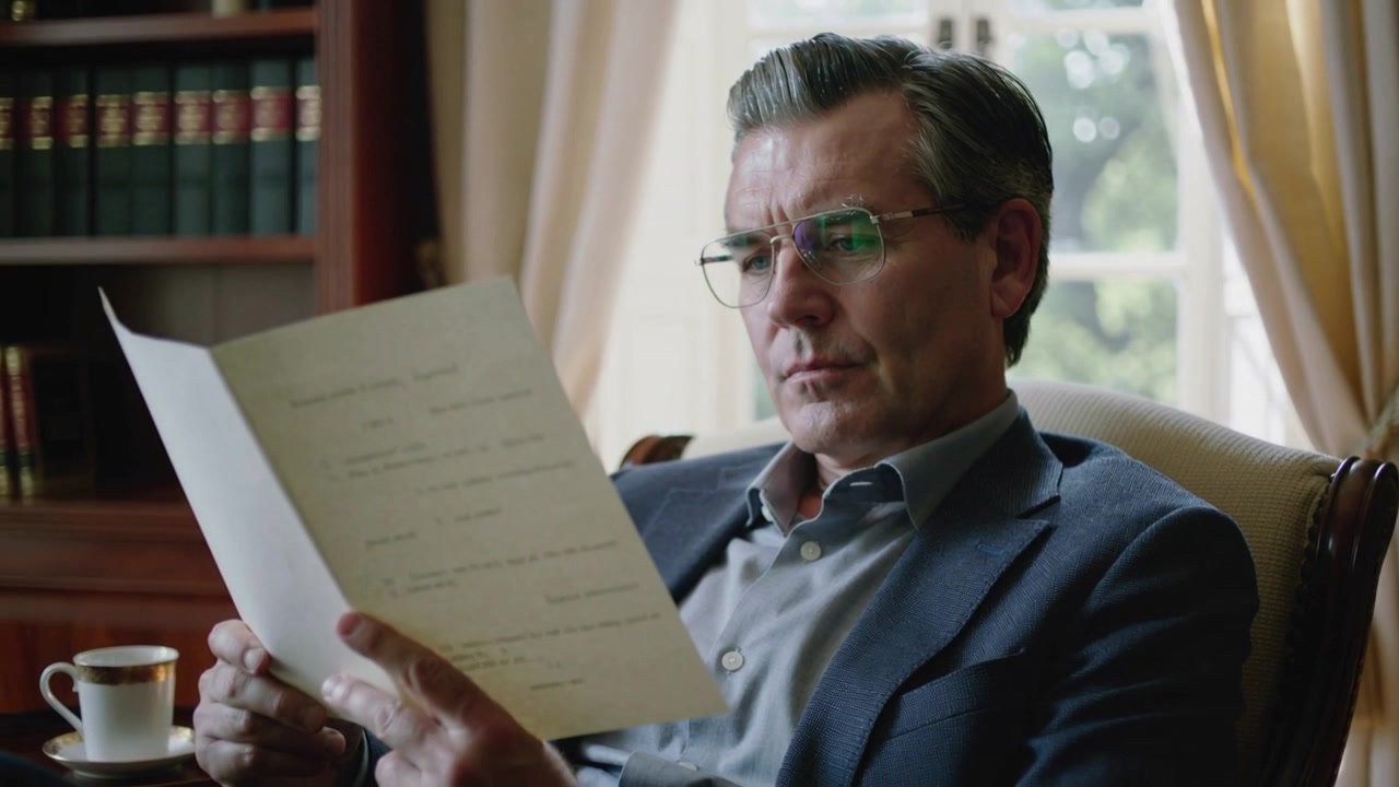 Tenendo un foglio grande, un uomo di mezza età in abito esamina un documento nello studio, rivedendo il contenuto per lavoro.