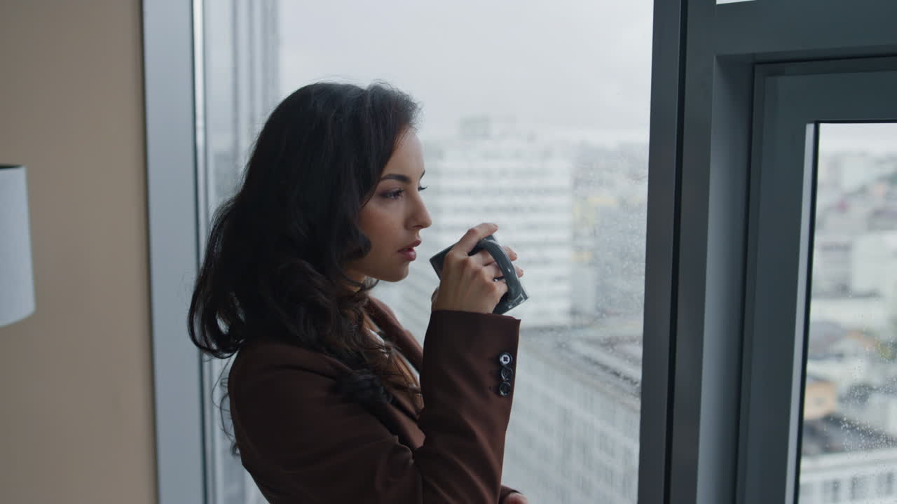 Woman manager drinking tea looking on cityscape from office window close up.