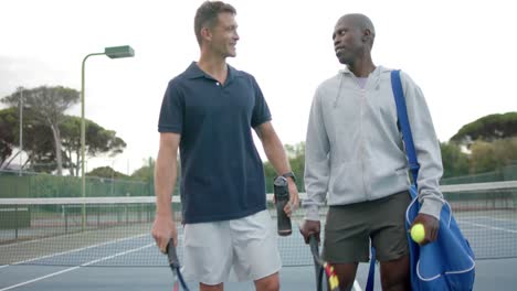 Happy-diverse-male-friends-walking-and-talking-on-outdoor-tennis-court,-slow-motion
