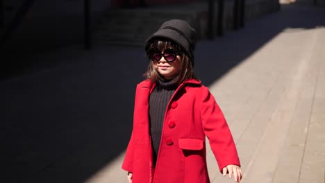 fashionable korean baby girl in a red coat walks down the street in spring