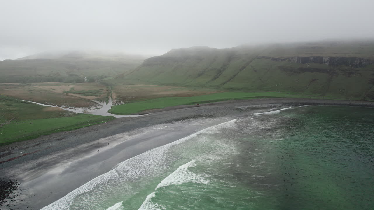 disparo aéreo de drones de olas en el océano atlántico rodando en una playa de grava en la bahía de talisker en escocia