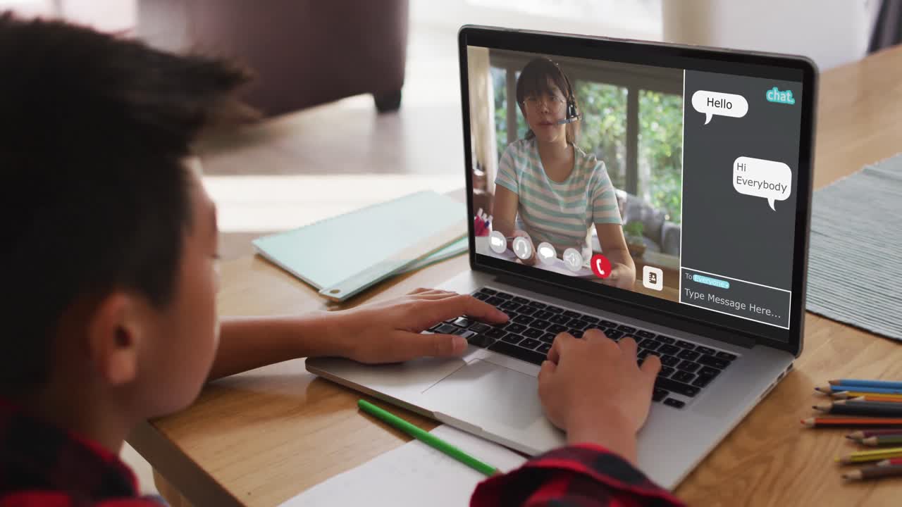 Schoolboy using laptop for online lesson at home, with female teacher talking and web chat on screen