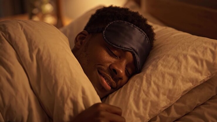 A peaceful moment captured as a young man peacefully sleeps, wearing a soft sleep mask and surrounded by fluffy white pillows, embracing tranquility in the comfort of his bed.