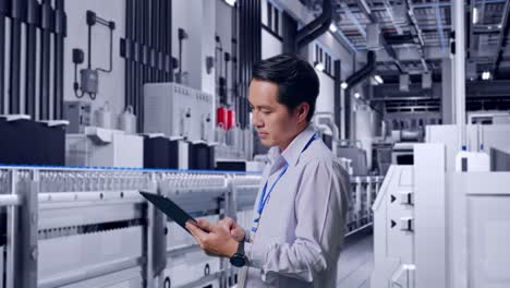side view of an asian male professional worker standing with his tablet with water production in bottling factory, checking on his tablet with meditation
