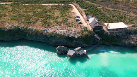 Luftaufnahme-Von-Einer-Drohne-Eines-Restaurants,-Das-Auf-Holzstelzen-über-Dem-Türkisfarbenen-Wasser-Einer-Klippe-In-Sansibar,-Tansania,-Thront