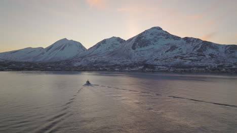 fisherman boat sailing to snowy fjord shore in norway at dusk, aerial