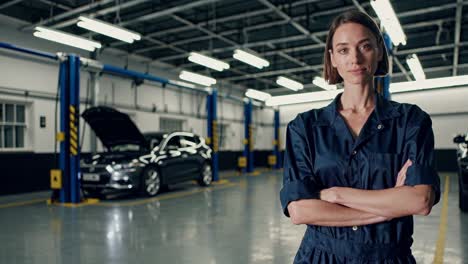 una mecánica profesional de pie con confianza con los brazos cruzados en un moderno taller de reparación de automóviles, un coche con un capó abierto visible en el fondo