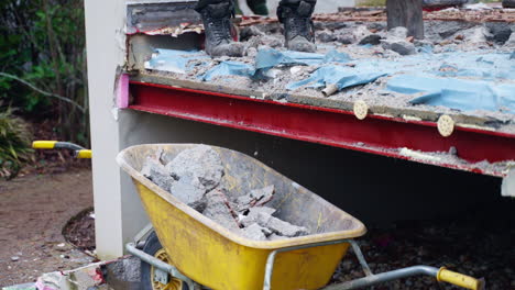 house construction site - men workers demolish concrete floor and shovel building waste in a wheelbarrow