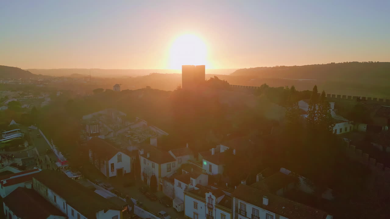 Pôr do sol realçando os telhados do centro histórico e a muralha antiga. Silhueta do castelo de Óbidos.